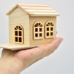 Mano sujetando una pequeña casa de madera con fondo blanco - a small wooden house with a small house