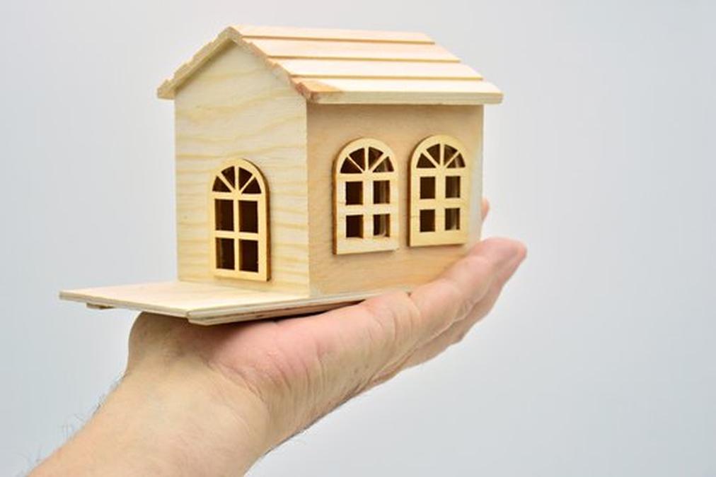 Mano sujetando una pequeña casa de madera con fondo blanco - a small wooden house with a small house