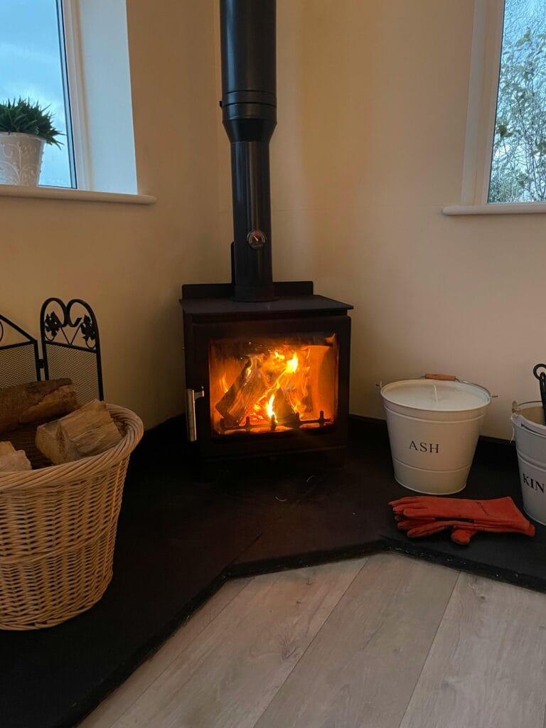 A warm and inviting room with a cozy fireplace, basket of firewood, and metal ash buckets.