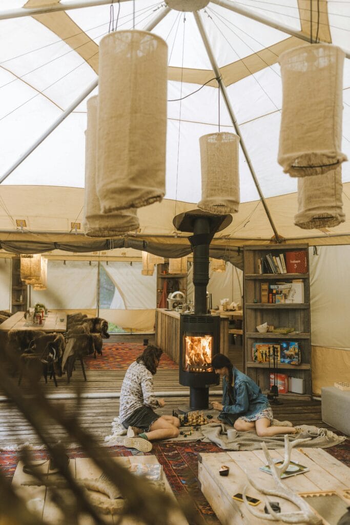 A warm glamping experience indoors, featuring a couple sitting by the fireplace in a modern tent.